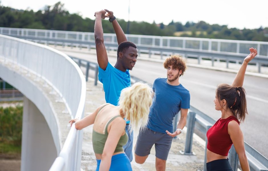 Quatro jovens praticando alongamento e exercícios ao ar livre em uma ponte, demonstrando motivação e saúde durante atividade física ao ar livre.
