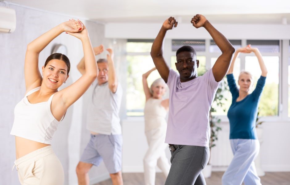 Grupo de pessoas idosas praticando alongamento e exercícios de alongamento em uma aula de fitness em um ambiente bem iluminado e moderno.